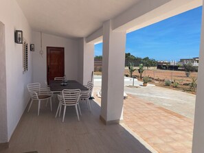 Eine überdachte Terrasse mit Esstisch und Stühlen, eine Holztür und Blick auf einen eingezäunten Garten.