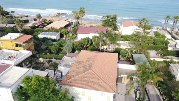 A coastal residential area with houses, some with red-tiled roofs, and a beach in the background. - Villa at Sea (Avola)