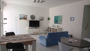A living room with a TV, sofa, dining table, chairs, and artwork on the walls. - Villa at Sea (Avola)