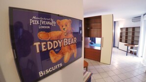 A room with a wall-mounted advertisement for Teddy Bear Biscuits, a wooden bookshelf, and a small table with a chair. - New, Spacious, Bright, Elegant Loft Apartment With Balcony. Opposite the Hospital S. Orsola (Bologna)