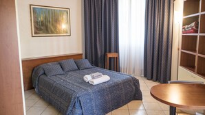 A hotel room with a bed, a small table, a wardrobe, and a painting on the wall. - New, Spacious, Bright, Elegant Loft Apartment With Balcony. Opposite the Hospital S. Orsola (Bologna)