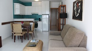 Een woonkamer met een beige bank, een rieten salontafel, en een eethoek met rieten stoelen en een kleine tafel.