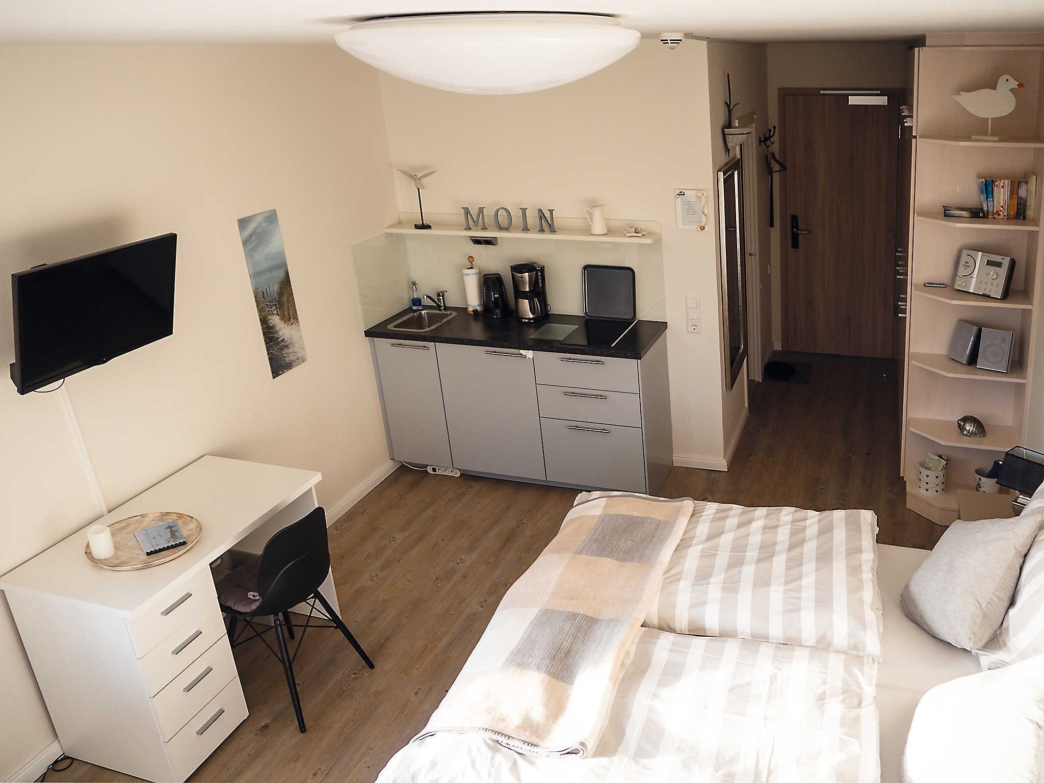 A compact bedroom with a bed, a desk, and a kitchenette.