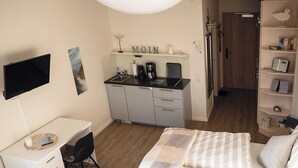 Une chambre compacte comprenant un lit, un bureau et un coin cuisine.