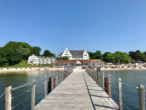 A wooden pier leading to a beach with a large hotel in the background. - Apartment Auszeit, Germany (Glücksburg (Ostsee))
