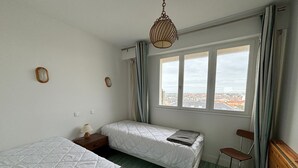 Habitació amb dos llits, una finestra que donava a edificis, un llum penjant i una cadira.
