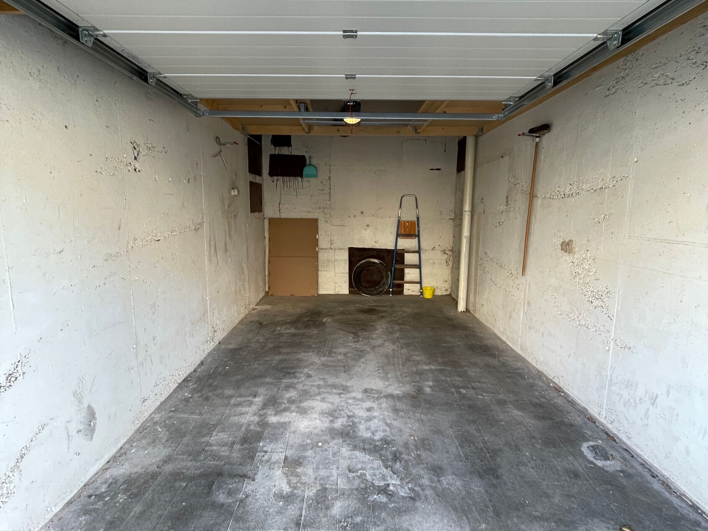 Un garage avec un sol en béton, une porte en bois, une échelle et un lave-linge.