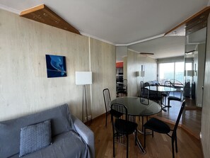 Quarto de hotel moderno com área de jantar, sofá e uma grande janela com vista.