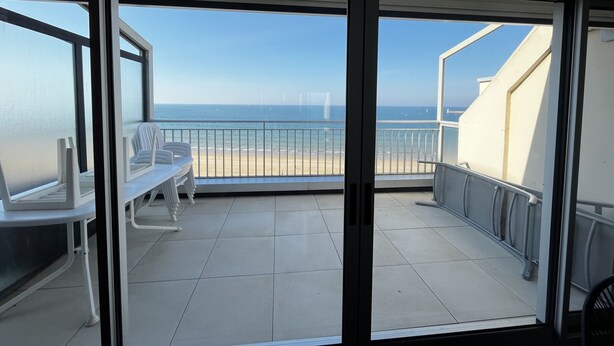 Un balcó amb vista a la platja i l'oceà. Hi ha cadires blanques i una taula al balcó.