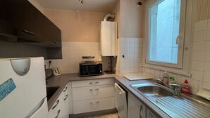 Una cuina senzilla amb armaris blancs, microones, rentapelats i una finestra.