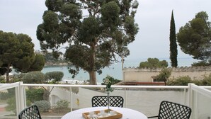 Un balcon avec une table préparée pour le thé, offrant une vue sur la côte, avec des arbres et un ciel dégagé.
