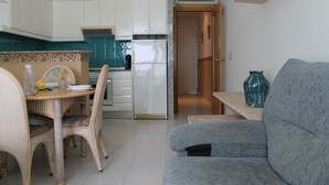 Une cuisine compacte avec des meubles blancs, un réfrigérateur encastré et un coin repas doté de chaises en osier.