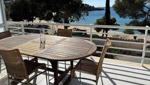 Ein runder Holztisch mit Korbstühlen auf einem Balkon mit Blick auf einen Strand und das Meer.