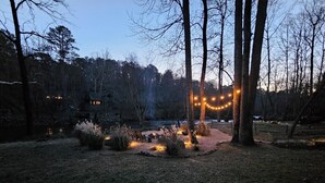 A backyard with a fire pit, string lights, and a small wooden structure. - Casa Del Rio | Ellijay, GA (Ellijay)