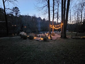 A backyard with a fire pit, string lights, and a small wooden structure.