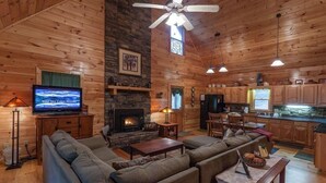 A cabin interior with a fireplace, wooden walls, a television, and a dining area. - Casa Del Rio | Ellijay, GA (Ellijay)