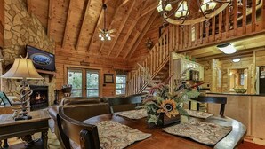A wooden cabin interior with a fireplace, dining table, and a large window. - Moonlight Hideaway | Ellijay, GA (Ellijay)