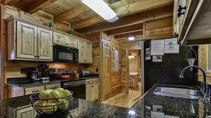 A kitchen with wooden cabinets, a black countertop, a sink, and a microwave. - Moonlight Hideaway | Ellijay, GA (Ellijay)