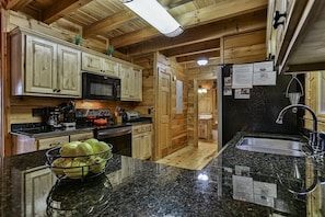 A kitchen with wooden cabinets, a black countertop, a sink, and a microwave. - Moonlight Hideaway | Ellijay, GA (Ellijay)