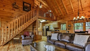 A wooden cabin interior with a staircase, a living room with a sofa and coffee table, and a kitchen area. - Moonlight Hideaway | Ellijay, GA (Ellijay)