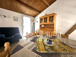 A dining area with a table set for four, a wooden cabinet, a sofa, and a window with curtains.