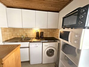 Eine kompakte Küche mit Mikrowelle, Kaffeemaschine, Geschirrspüler und Waschmaschine.