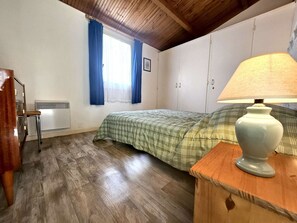 A bedroom with a bed, a chair, a lamp, a radiator, and a window with curtains.