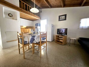 A dining area with a table and chairs, a kitchen with appliances, a television, and a framed picture on the wall.