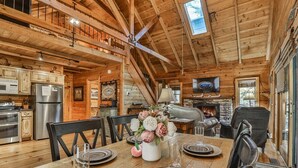 A wooden cabin interior with a dining table set, kitchen appliances, and a fireplace. - Hemlock Creek | Cherry Log, GA (Cherry Log)