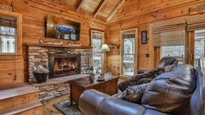 A cabin interior with a stone fireplace, leather sofa, wooden walls, and a mounted sign for Blue Sky Cabin Rentals. - Hemlock Creek | Cherry Log, GA (Cherry Log)