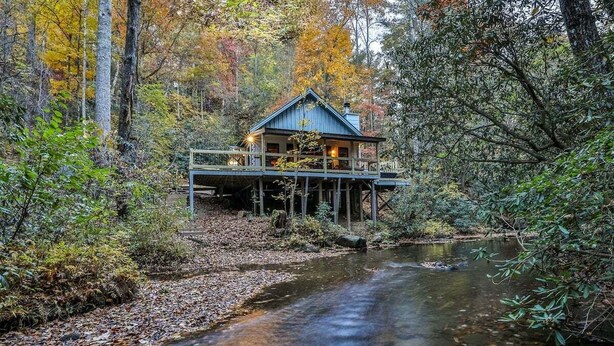A cabin with a deck overlooking a river, surrounded by autumn foliage. - Hemlock Creek | Cherry Log, GA (Cherry Log)