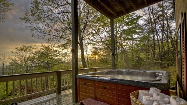 Ein Whirlpool auf einer Holzterrasse mit Blick auf Bäume und einen Sonnenuntergang.