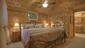 Ein Schlafzimmer einer Holzhütte mit Bett, Nachttischen, Lampen, Deckenventilator und Spiegel.