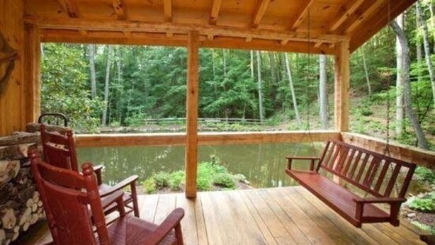 Eine Holzterrasse mit Bank und Stühlen mit Blick auf einen Teich, der von einem Wald umgeben ist.