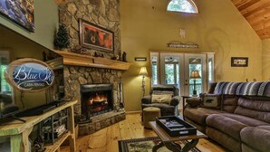 Een gezellige woonkamer met een stenen openhaard, een bank, een televisie en een bord met de tekst Blue Sky Cabin Rentals.