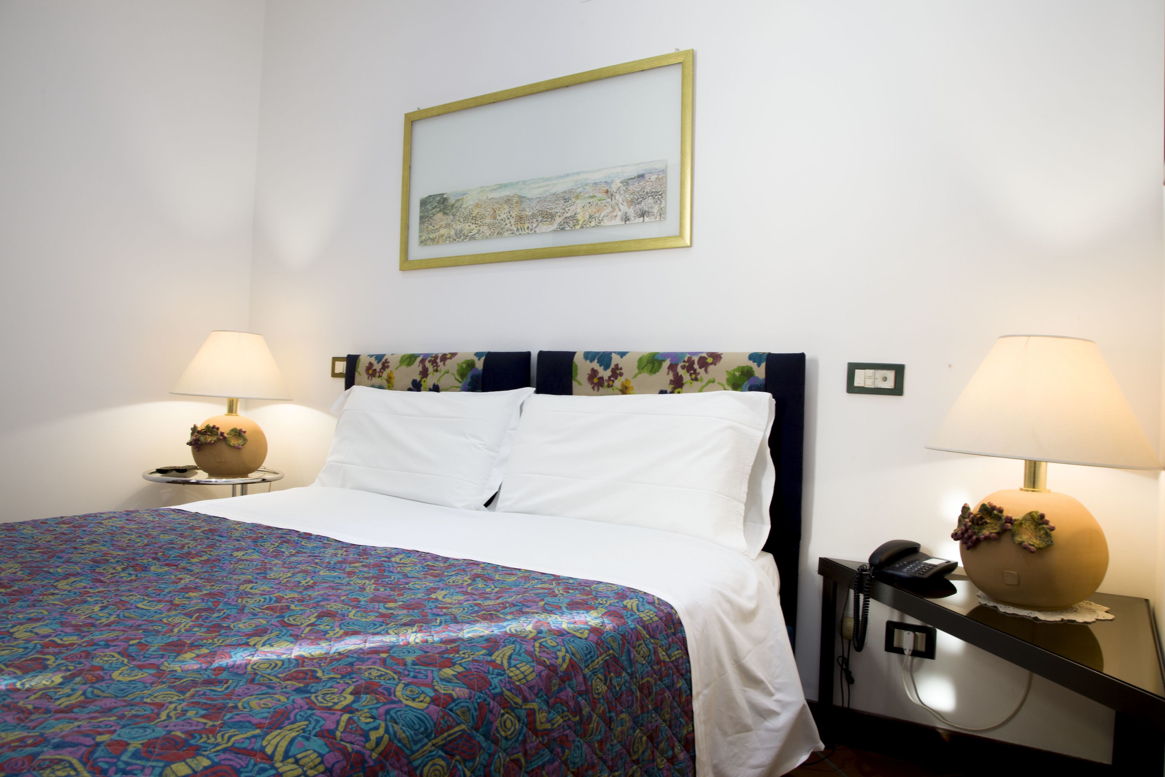 A hotel room with a large bed, two bedside tables with lamps, a framed picture on the wall, and a patterned bedspread.
