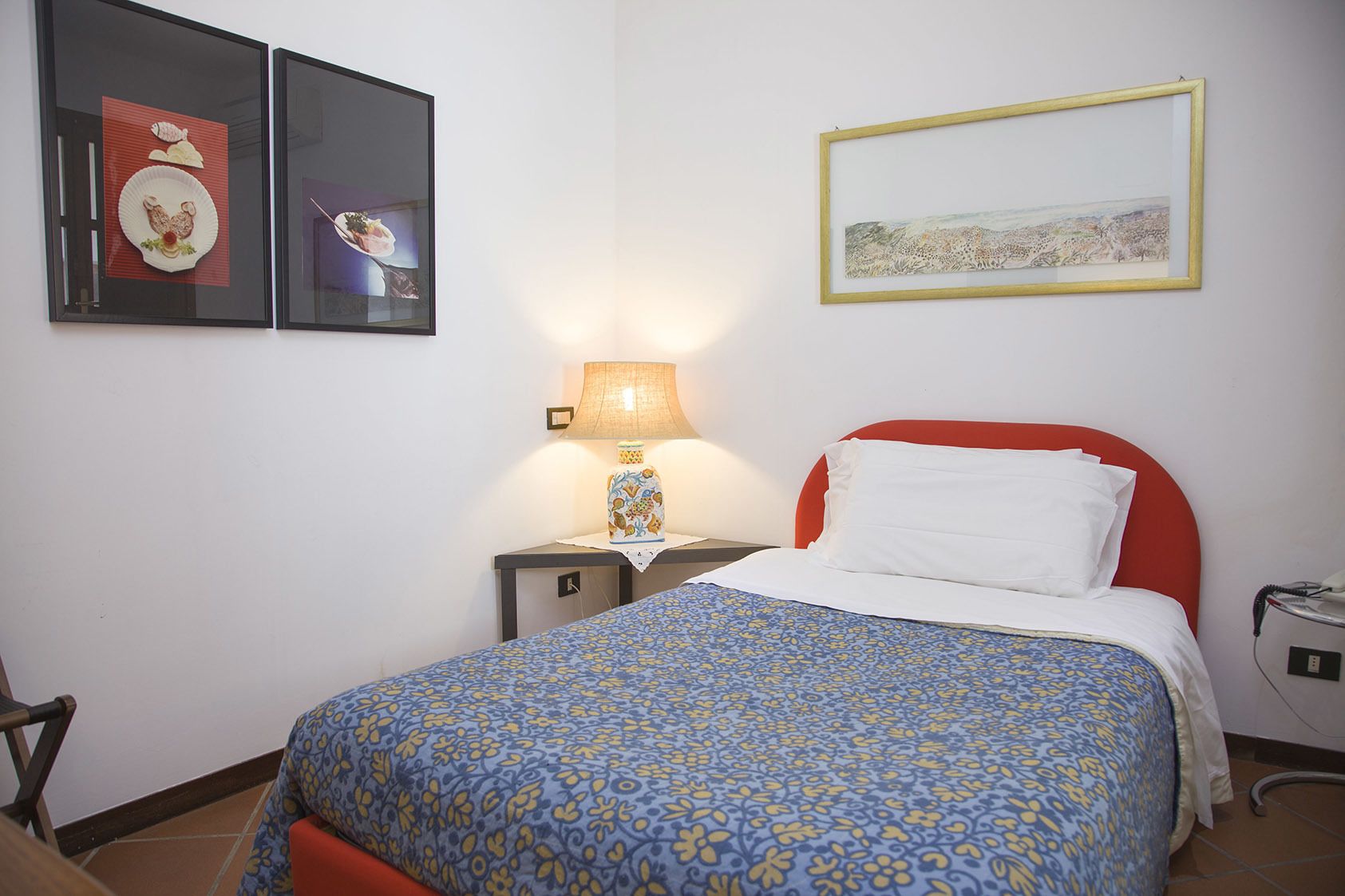 Une chambre d’hôtel avec un lit, une table de chevet, une lampe et deux tableaux encadrés au mur.
