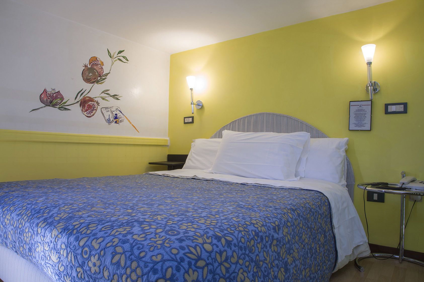 Una habitación de hotel con una cama, una mesita de noche, una lámpara y un adorno en la pared.