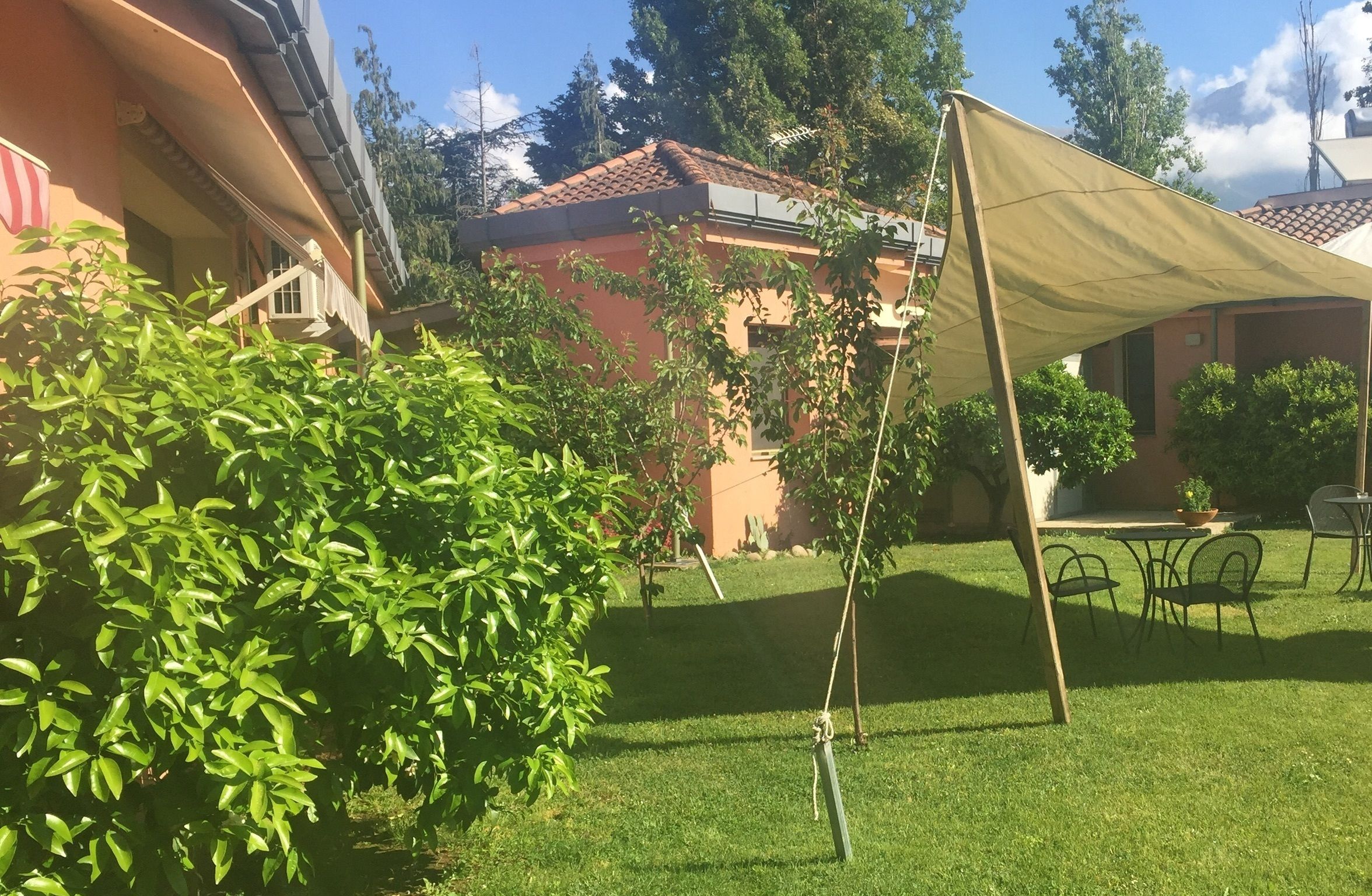 A courtyard with a lawn, a table with chairs, and a building with a tiled roof.