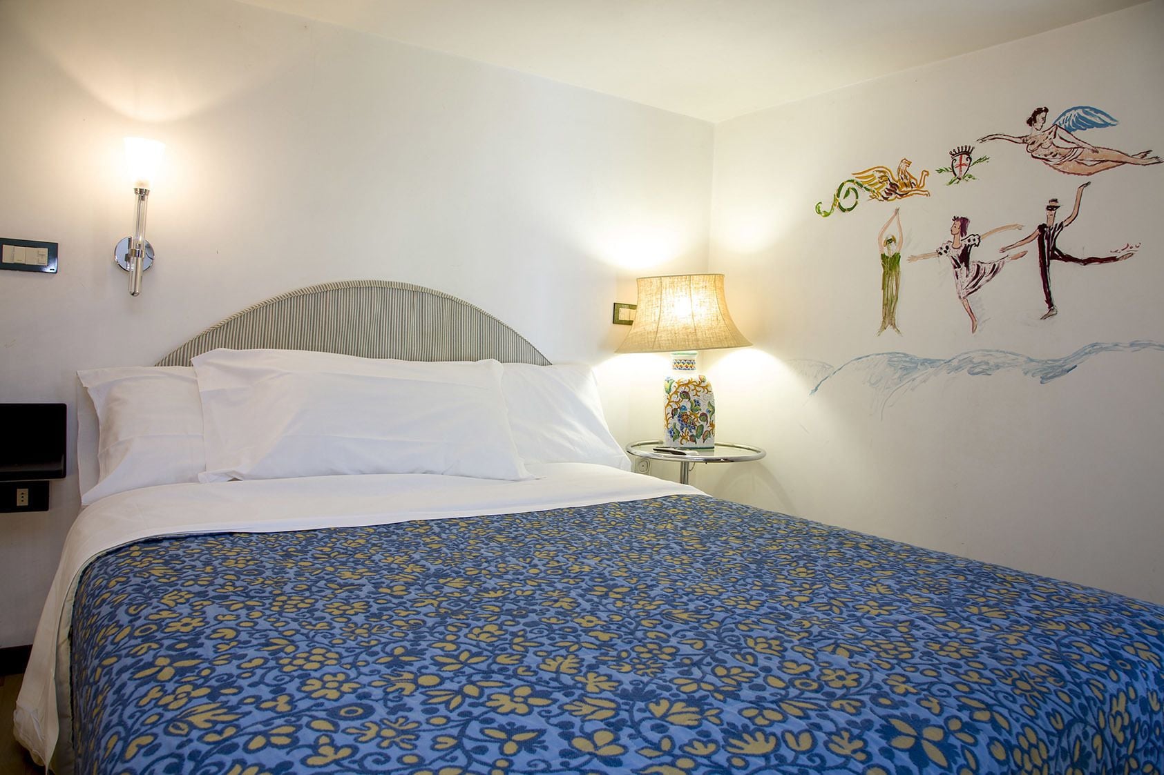 Ein Hotelzimmer mit Bett, Nachttisch mit Lampe und Wandbild.