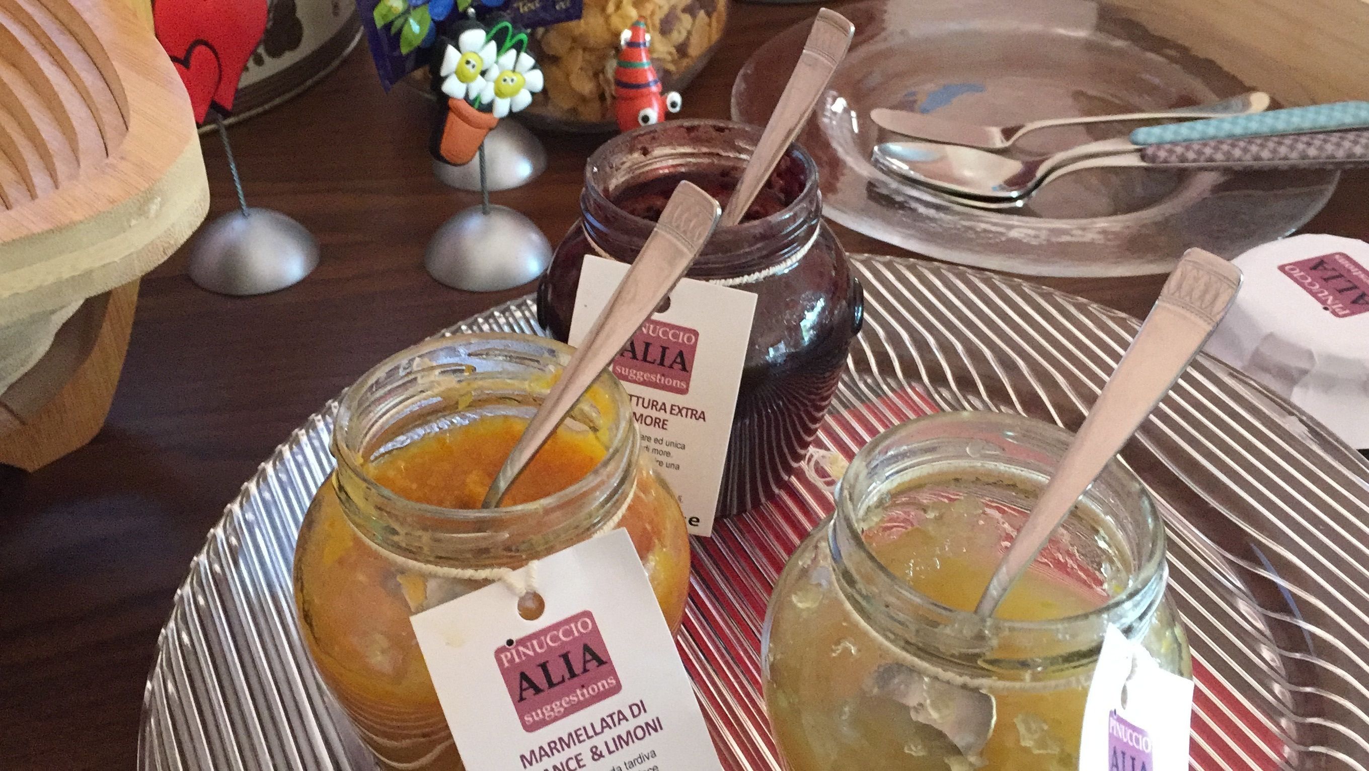 A table with jars of marmellata di frutta & limoni, a jar of chocolate spread, and a jar of orange marmalade.