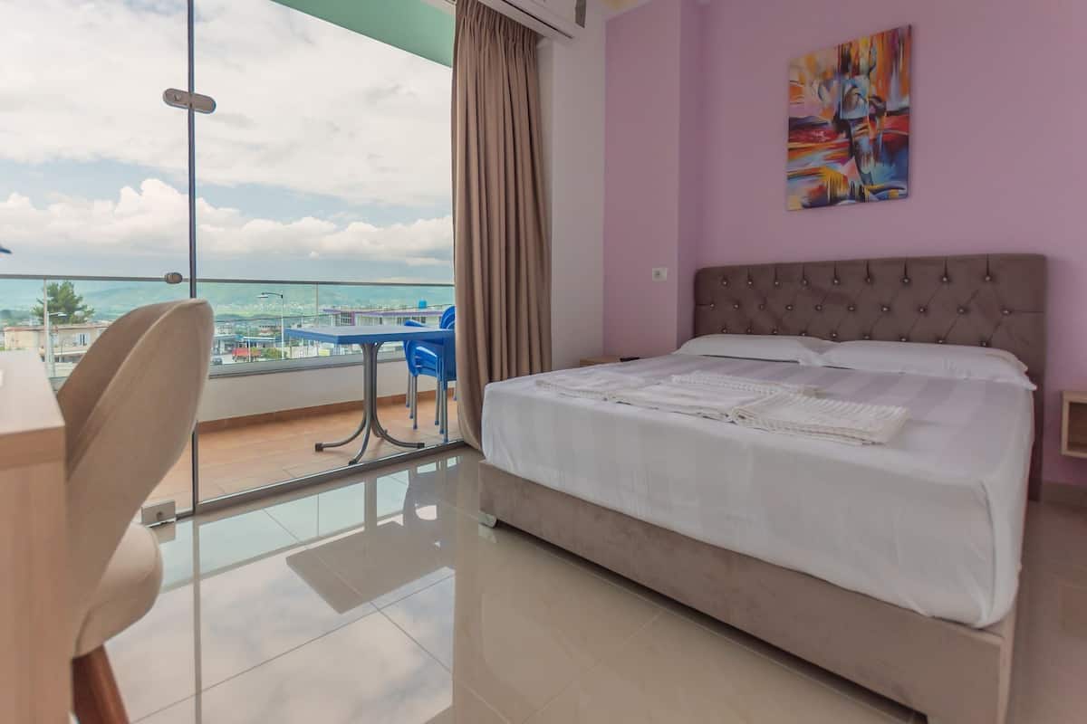 A hotel room with a large bed, a view of the city, and a balcony with a table and chairs.