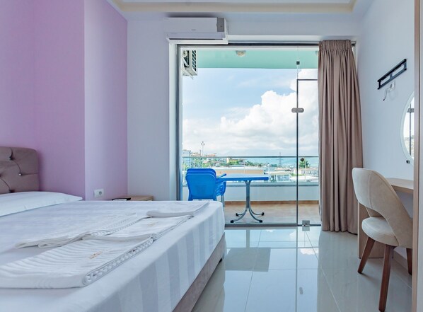A hotel room with a bed, a desk, a chair, and a view of the city through a large window. - The City Gate Hotel (Sarandë)