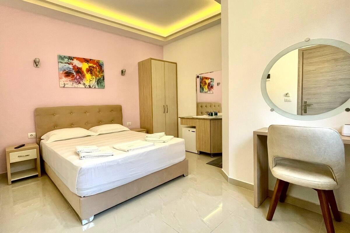 A bedroom with a bed, nightstands, a desk, a chair, a wardrobe, and a mirror.