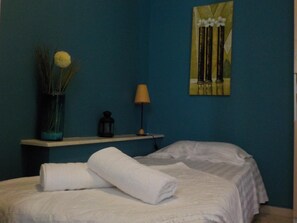 A hotel room with teal walls, a bed with white linens, a vase with dried plants, a lantern, and a painting of flowers. - Marysplacestalis (Hersonissos)