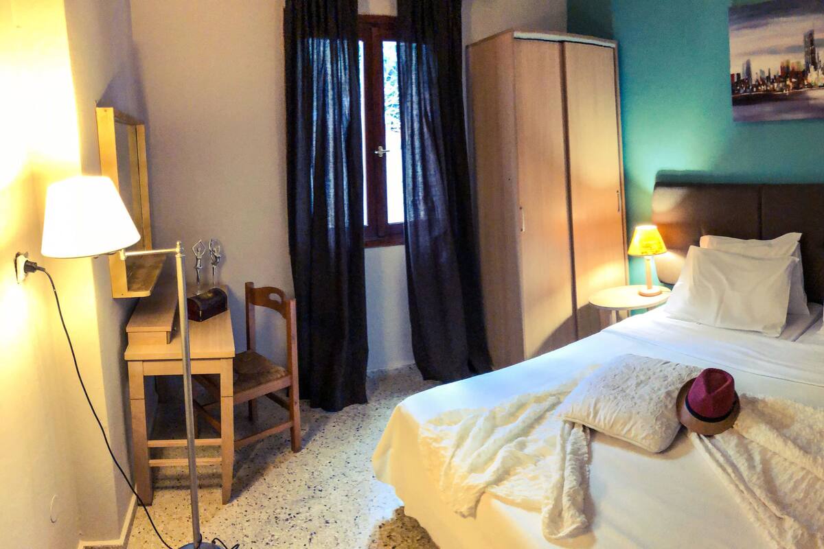 A hotel room with a bed, two bedside tables, a chair, a wardrobe, and a window with curtains.