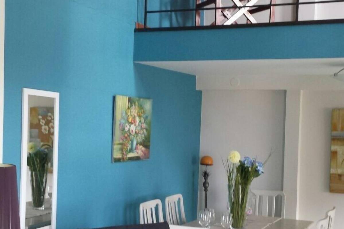 A dining area with a high ceiling, a balcony, and a painting on the wall.