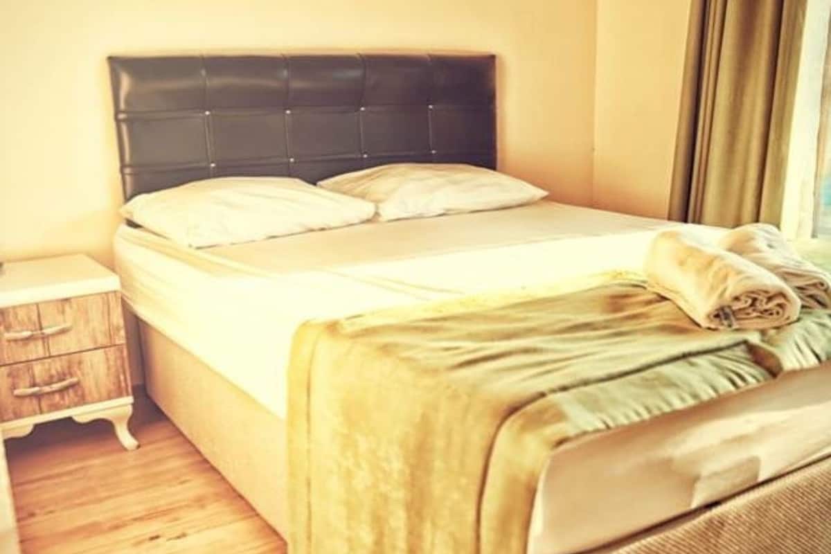 A bed with a headboard, a wooden nightstand, and a window with curtains.