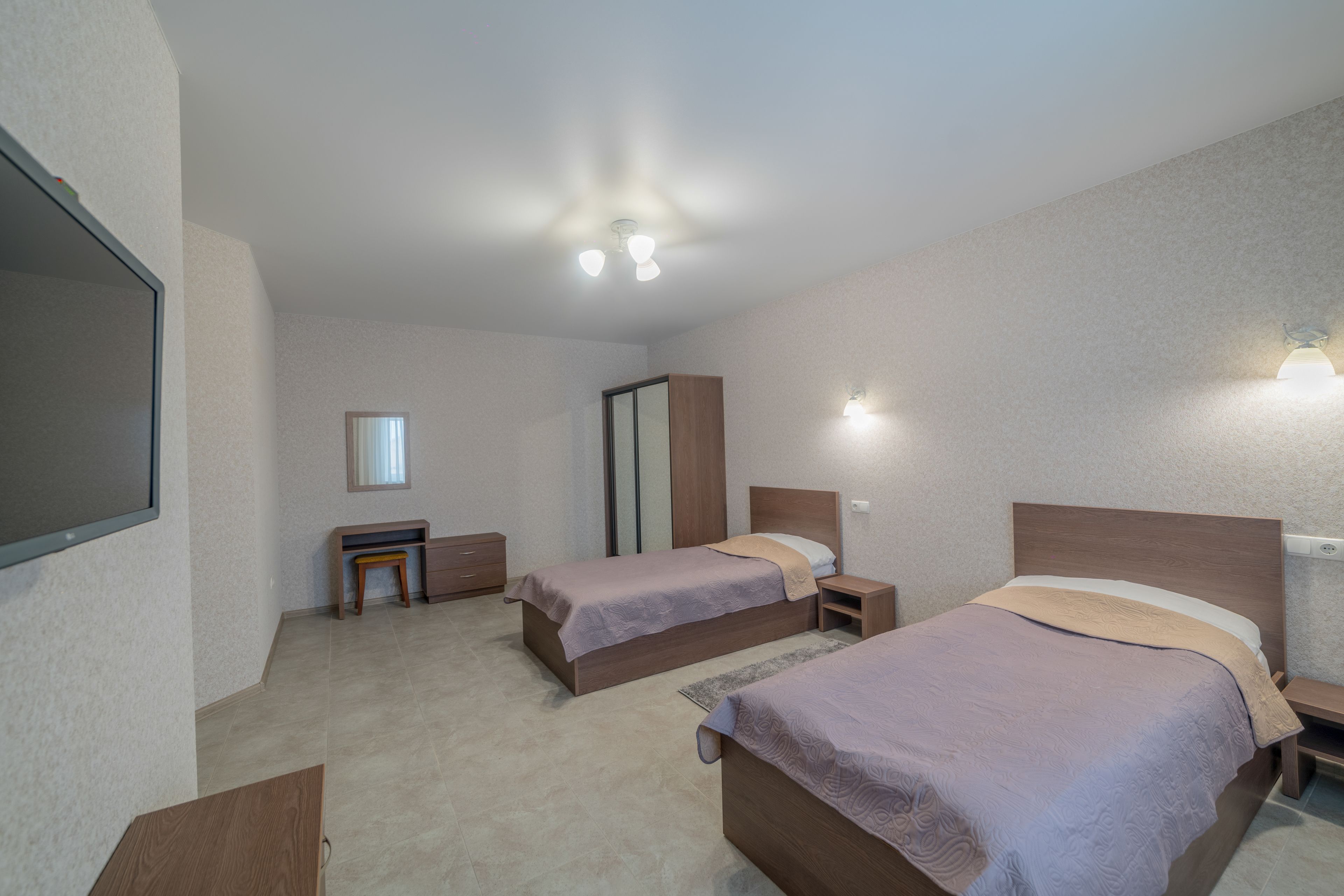 A hotel room with two beds, a desk, a mirror, and a TV.