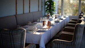 Un comedor con una larga mesa dispuesta para una comida, sillas tapizadas y vistas a través de grandes ventanales.
